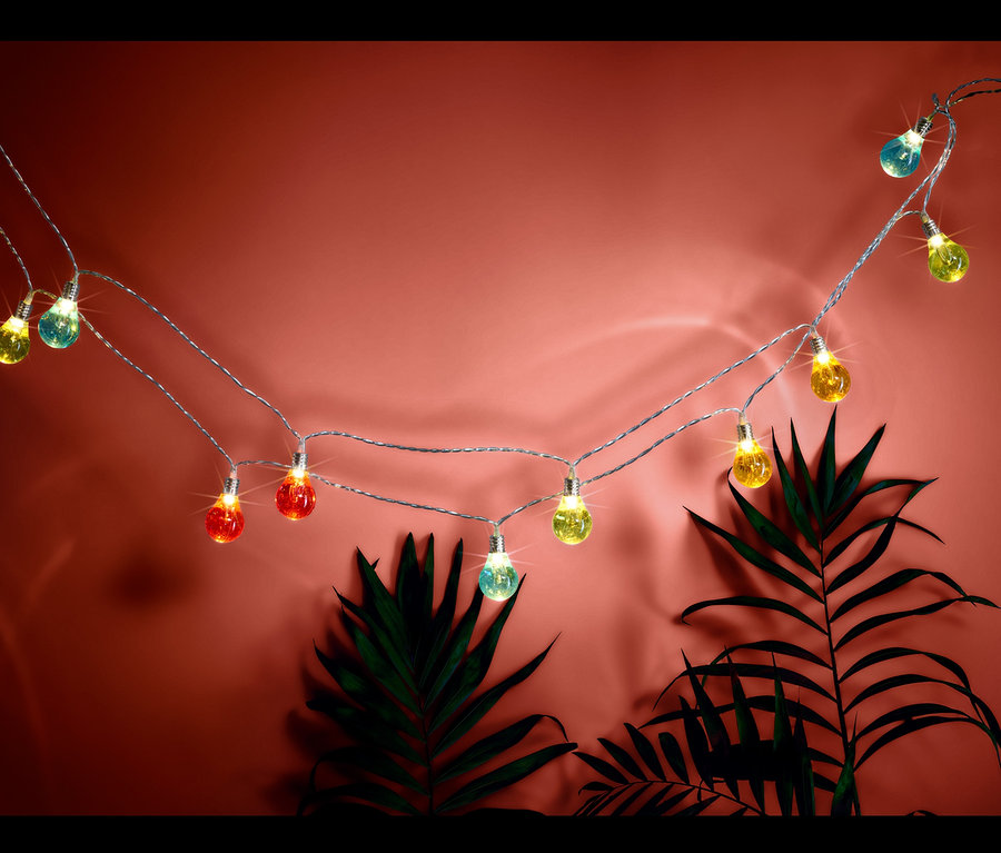 Eine LED-Lichterkette mit bunten Glühbirnen vor einem Hintergrund mit Pflanzen.
