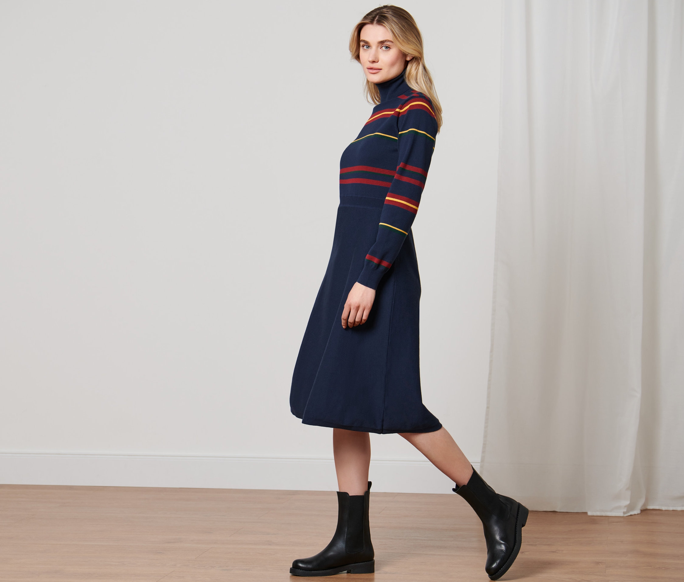 Frau geht und trägt ein Strickkleid und schwarze Stiefel.