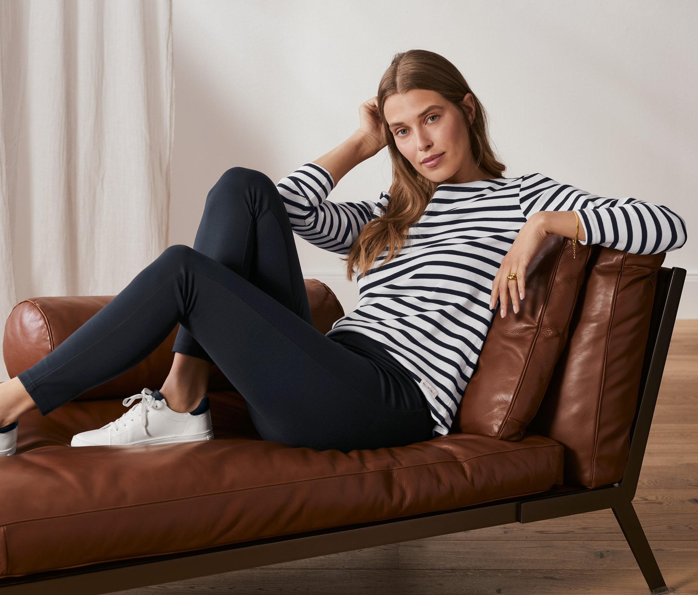 Frau sitzt auf Ledersessel, trägt dunkelblaue Basic-Leggings aus Heavy-Jersey.