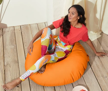 Frau sitzt auf orangefarbenem Vestio-Outdoor-Bodenkissen und trägt Leggings mit Obstmuster.