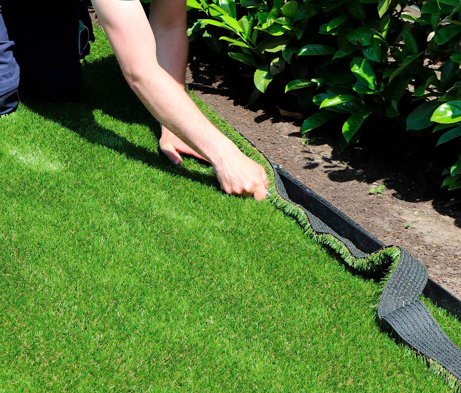 Mann verlegt Primaflor Kunstrasen »ARIZONA« entlang eines Gartenrandes.