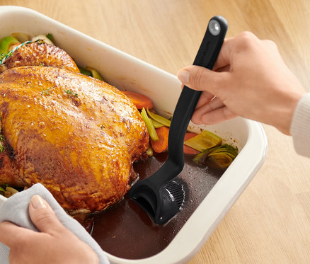 Hände bestreichen ein Brathähnchen in einer Auflaufform mit einem Back-und-Braten-Pinsel.