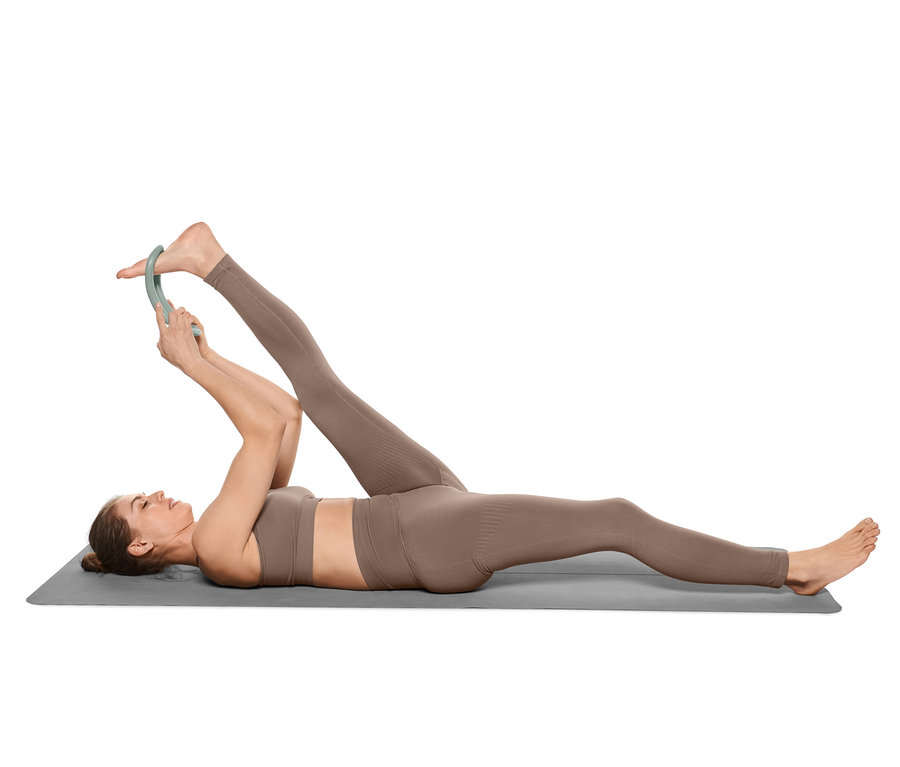 Frau liegt auf einer Matte und dehnt ihr Bein mit einem Yoga-Stretchring.