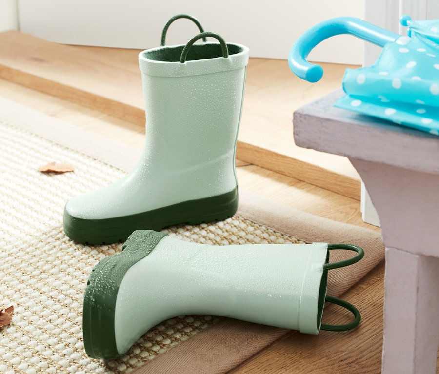 Grüne Gummistiefel stehen auf einer Fußmatte neben einem blauen Regenschirm.