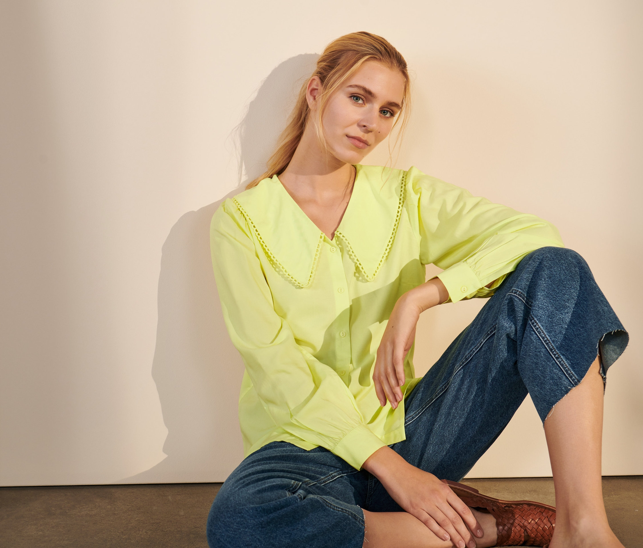 Frau sitzt am Boden und trägt eine Bluse mit Kragen.