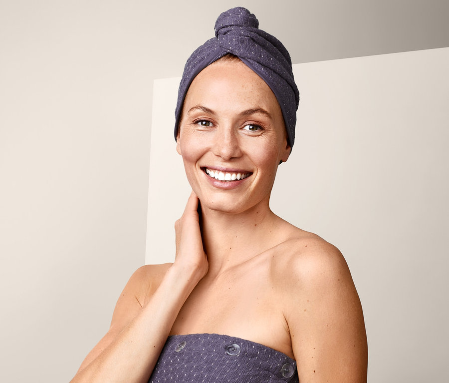 Frau lächelt mit Turban-Handtuch auf dem Kopf.