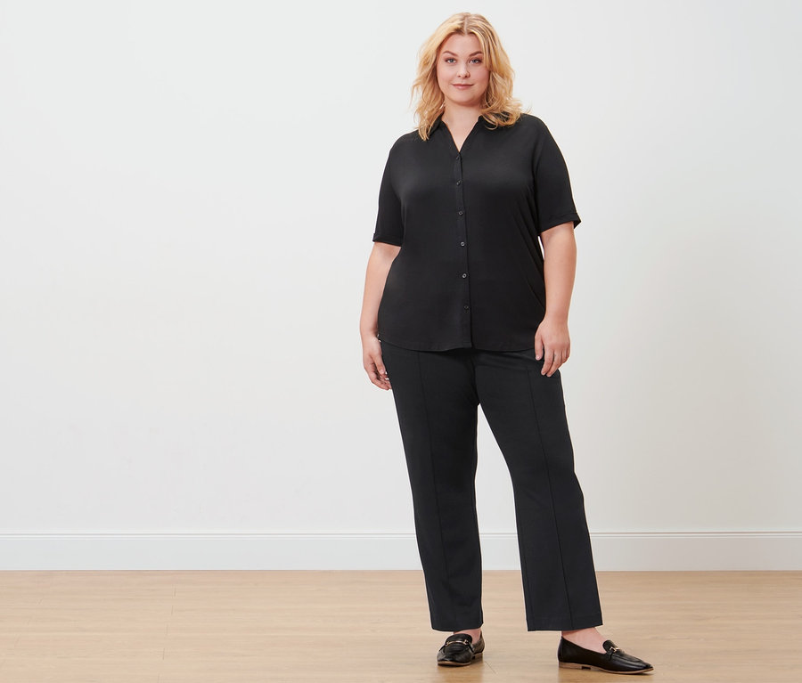 Frau posiert in schwarzem Blusenshirt mit Knopfleiste und schwarzer Sweathose.