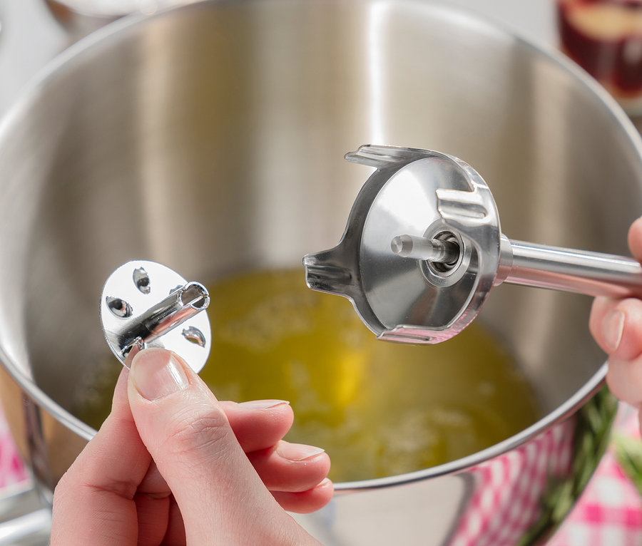 Frau befestigt einen Aufsatz an einem CASO Stabmixer »HB 2400 Pro XL« aus Metall über einer Schüssel mit Flüssigkeit.