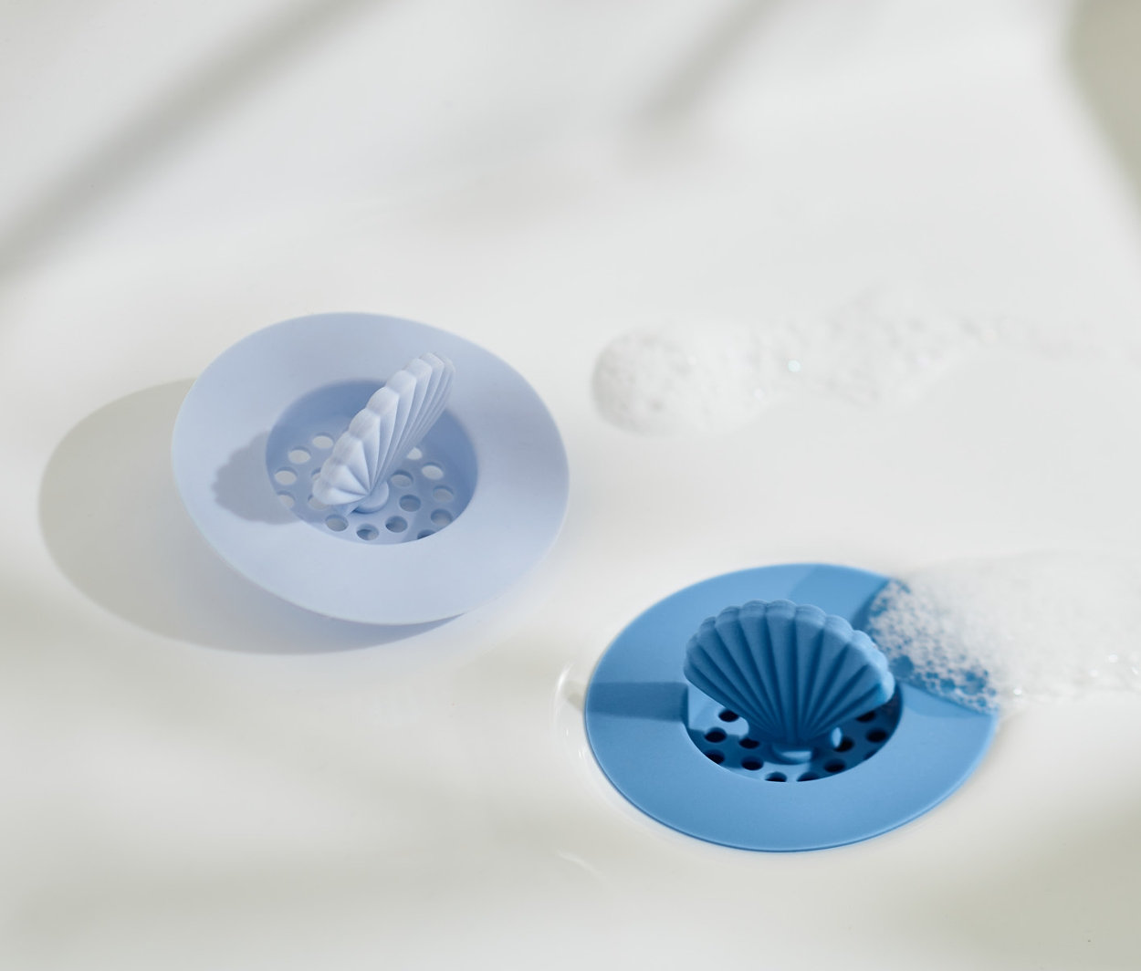 Zwei Abflusssiebe aus Silikon im Waschbecken. Ein hellblaues und ein blaues.