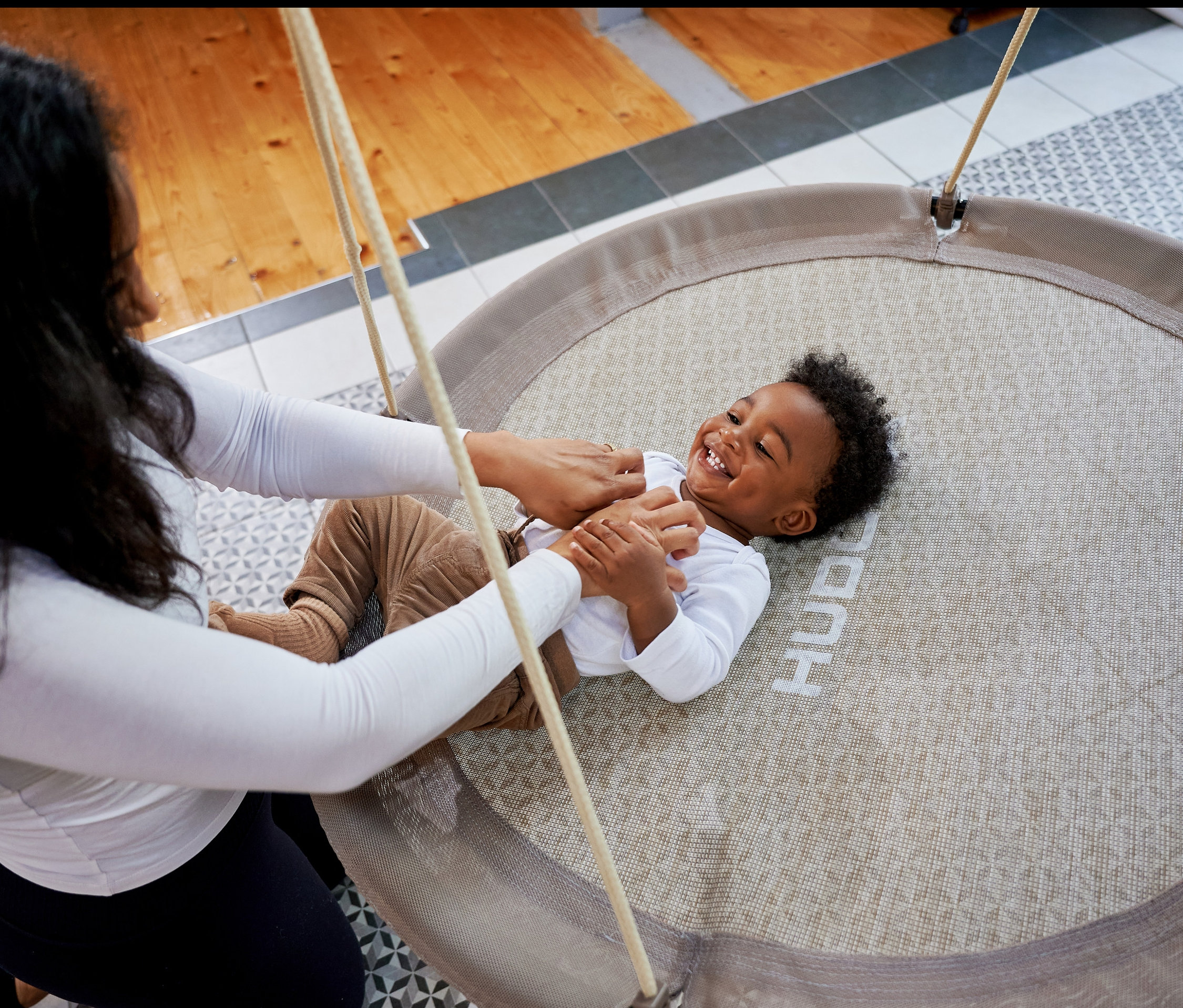 Mutter spielt mit Kind, das in beiger HUDORA Nestschaukel »Lounge« liegt.