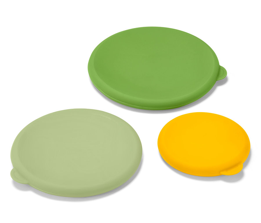 Drei Silikon-Frischhaltedeckel in Grün, Hellgrün und Gelb liegen auf einer weißen Oberfläche.