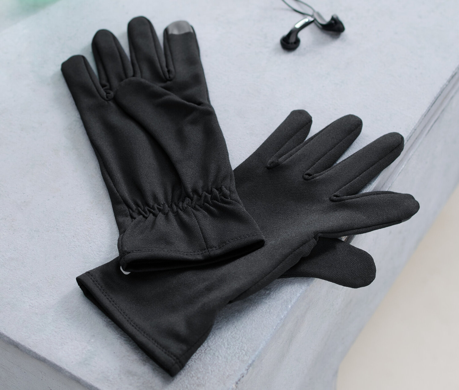 Laufhandschuhe, eine Wasserflasche und Kopfhörer liegen auf einer Bank.