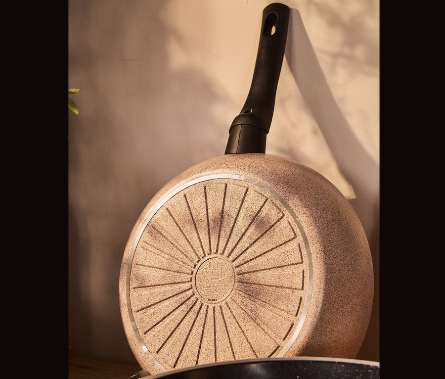 Nahaufnahme einer BALLARINI Aluminium-Bratpfanne, sand, mit schwarzem Griff von unten.