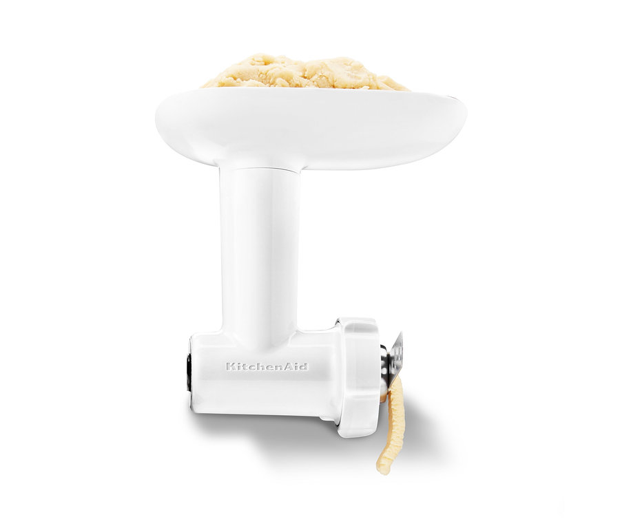 Detailansicht eines KitchenAid Fleischwolfaufsatzes mit Teig darin und Teig, der herauskommt.