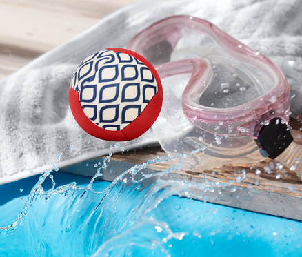 Ein hüpfender Wasserball liegt neben einem Handtuch und einer Schwimmbrille am Poolrand.