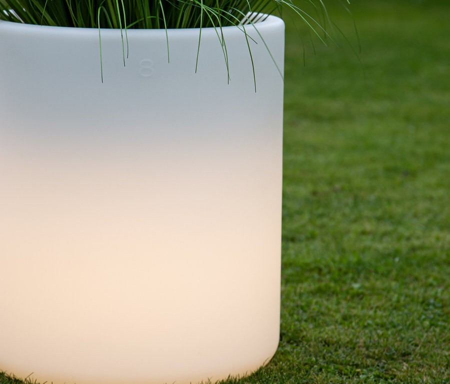 Eine weiße 8 seasons design LED-Leuchte steht im Gras, mit Pflanzen oben drauf.