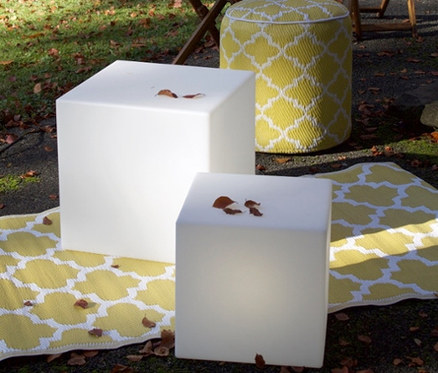 Zwei weiße Solar-Würfel und ein gelber Hocker auf einem gelben Teppich im Freien.