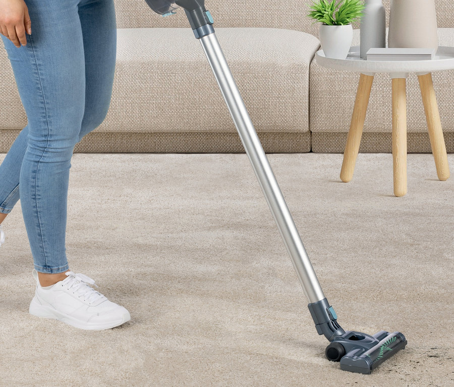 Frau saugt beigen Teppich mit Akku-Hand- und Bodenstaubsauger.