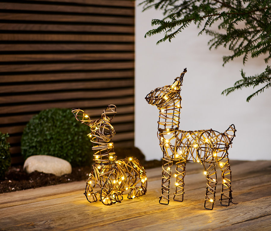 Zwei LED-Rentiere stehen auf einem Holzboden, eines liegt und das andere steht, beide leuchten.