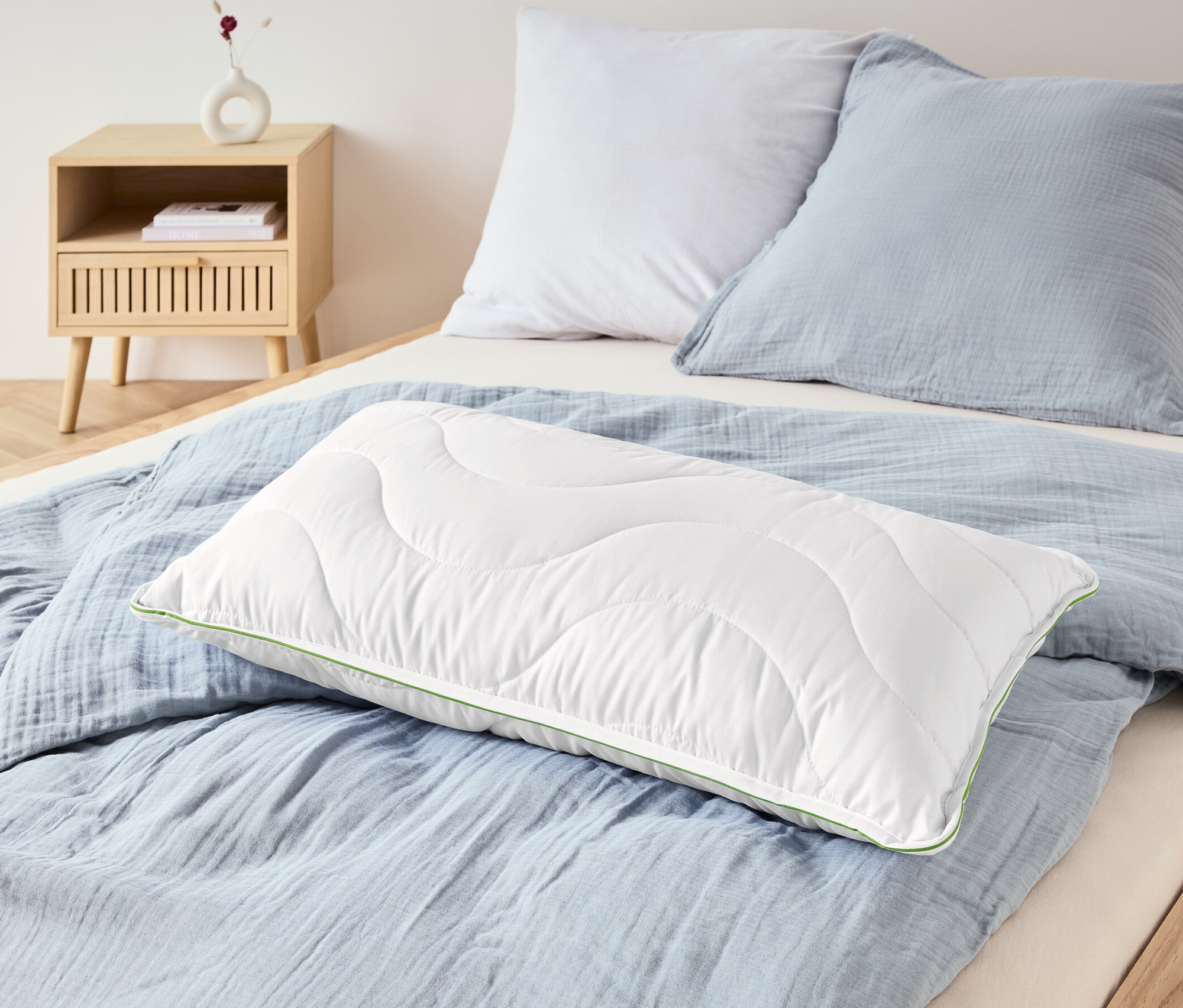 Auf einem Bett liegen zwei irisette® greenline Kopfkissen mit Dacron®-Aktivkohle und eine hellblaue Bettwäsche.
