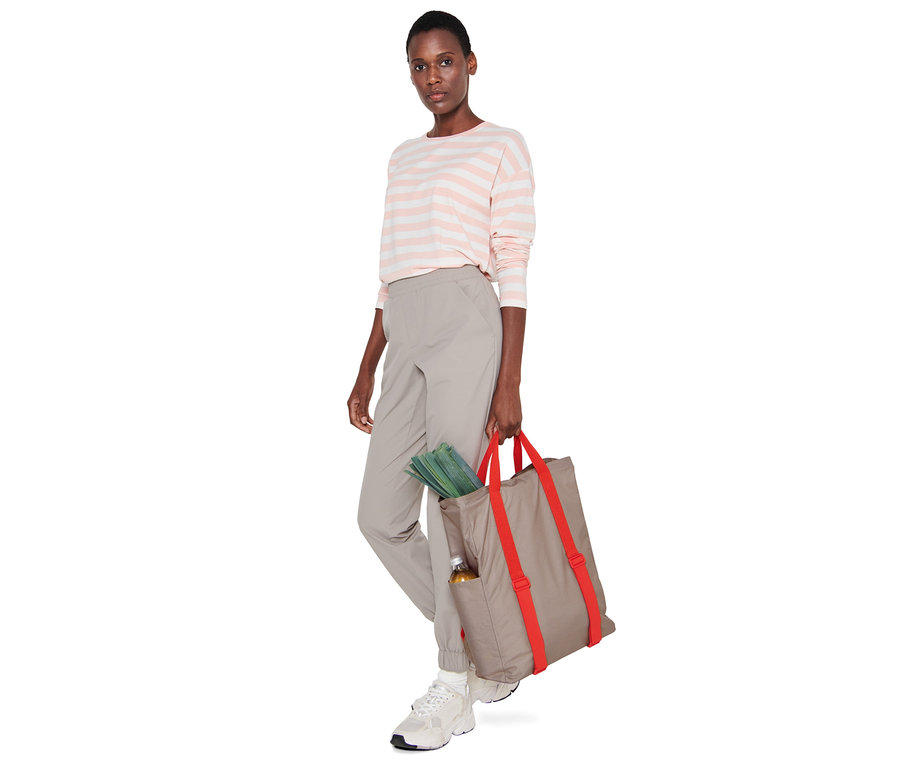 Frau hält einen Picknickrucksack, aus dem Gemüse und eine Flasche ragen.