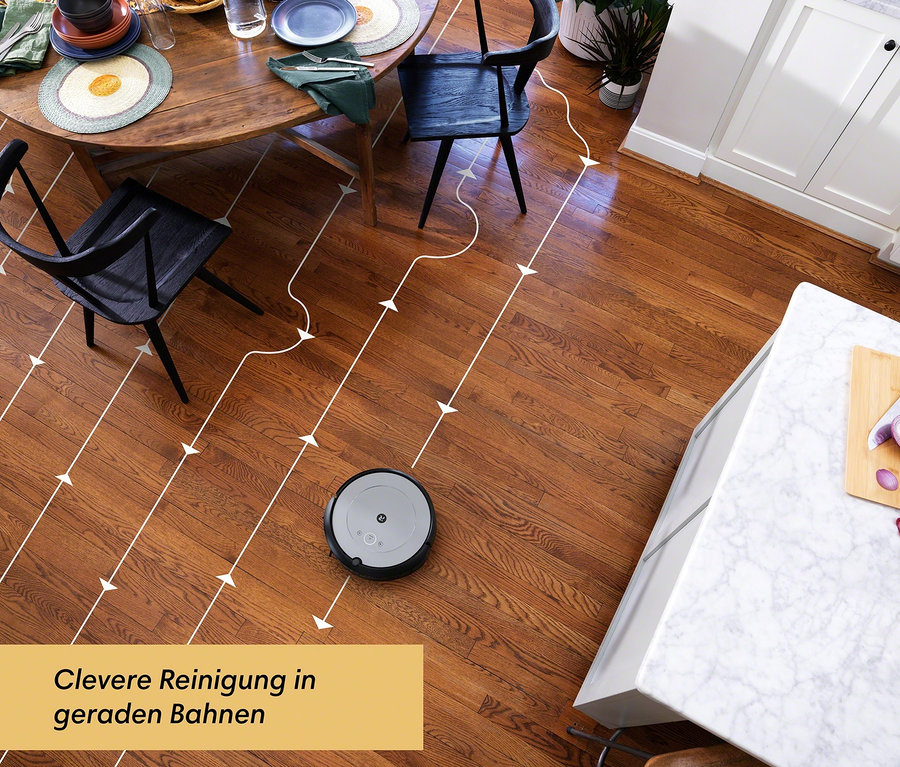 Ein grauer iRobot Roomba i1 Saugroboter reinigt einen Holzboden in einem Ess- und Küchenbereich.