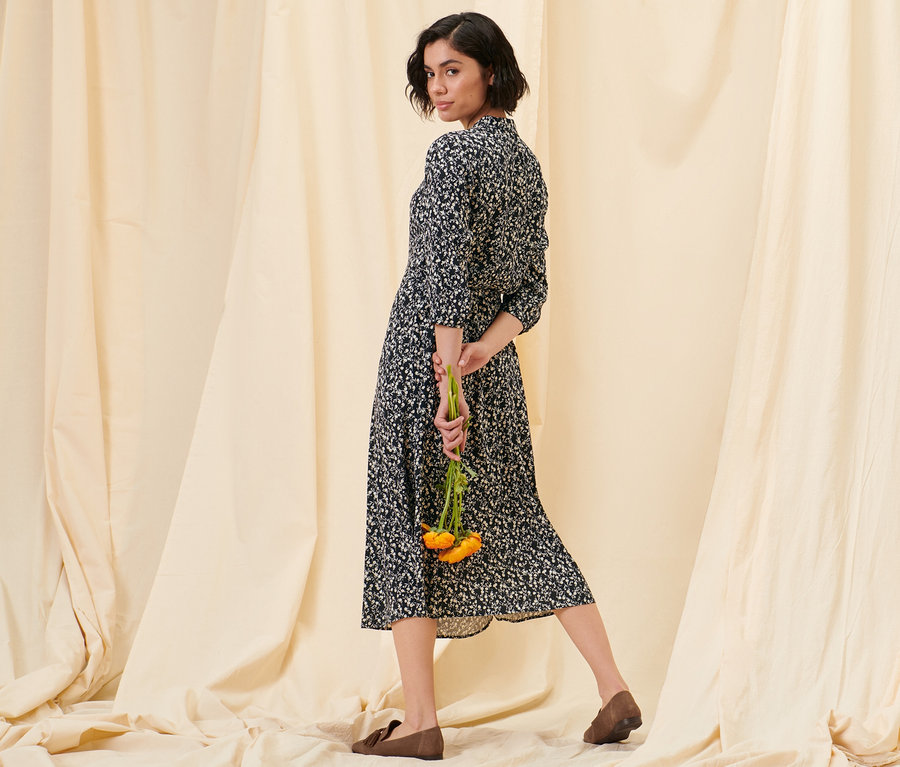 Frau posiert in einem floralen Hemdblusenkleid und Loafern aus Veloursleder.