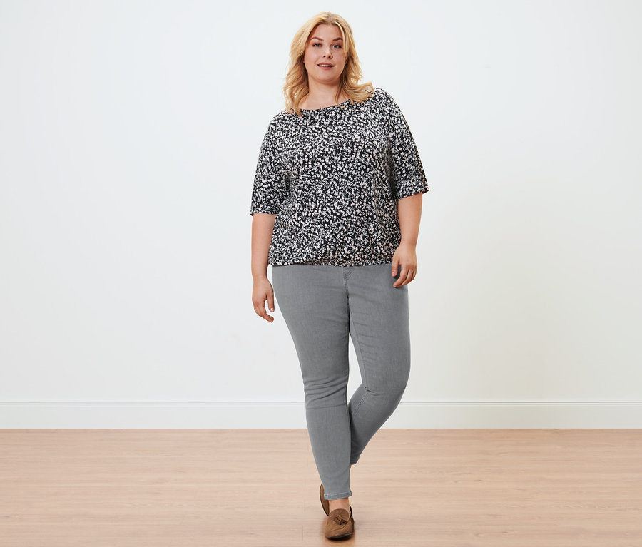 Frau posiert in einem geblümten Blusenshirt, hellgrauen Treggings und Veloursleder-Loafern.