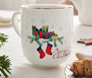 Nahaufnahme eines Jumbobechers mit Glanzgolddekor und Weihnachtsmotiv auf einem festlich gedeckten Tisch.