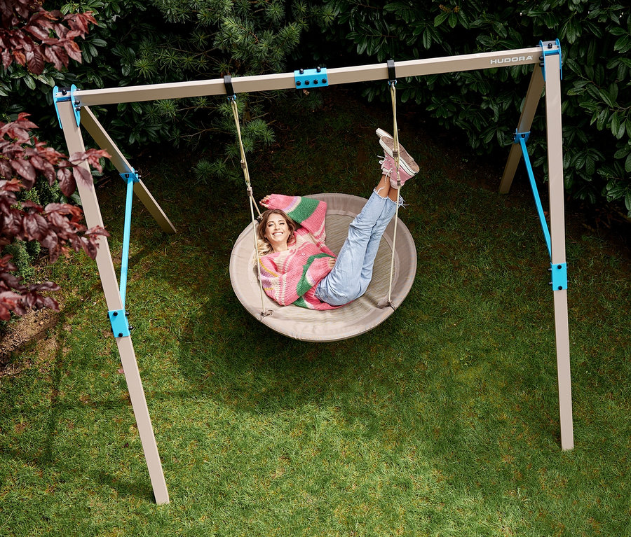 Eine junge Frau liegt in einer beige-farbenen HUDORA Nestschaukel »Lounge« mit einem Durchmesser von 110 cm im Garten.