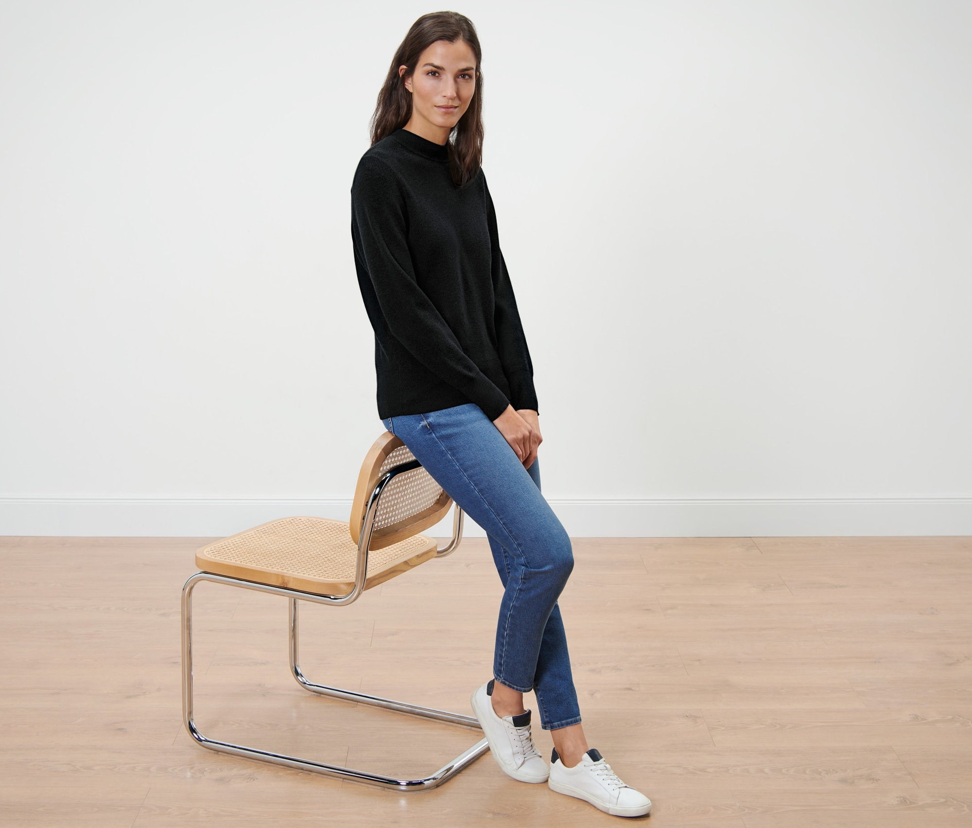 Frau sitzt auf einem Stuhl und trägt einen schwarzen Feinstrickpullover.