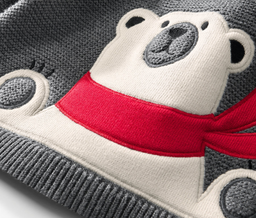 Detailaufnahme eines Kinder-Strickpullovers mit Eisbär-Applikation und rotem Schal.