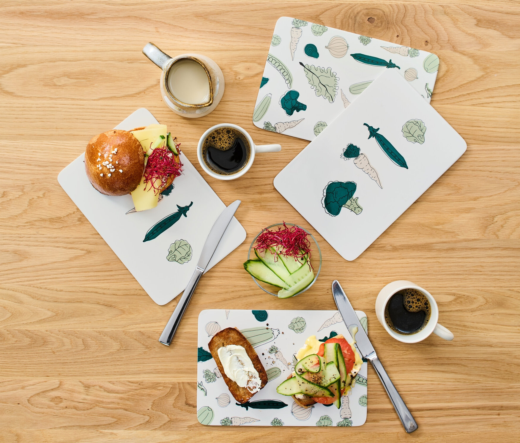 Frühstücksbretter mit belegten Broten, Kaffee und Milch auf einem Holztisch.