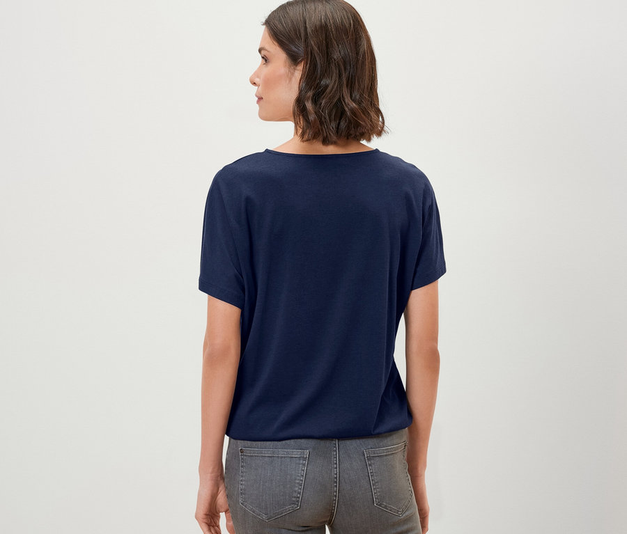 Rückansicht einer Frau mit einem dunkelblauen Blusenshirt und grauen Jeans.