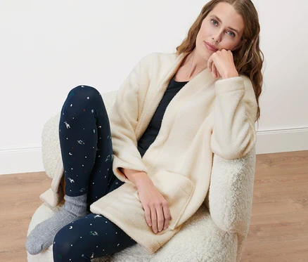 Frau sitzt in einem Sessel und trägt eine Teddyjacke.
