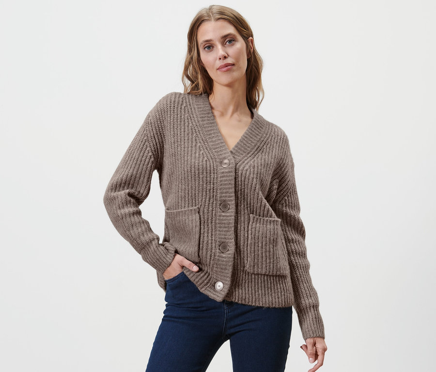 Frau posiert in Grobstrick-Cardigan mit Wolle und dunkelblauen Jeans.