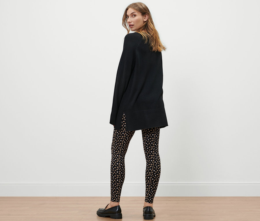 Eine Frau steht mit dem Rücken zur Kamera und trägt ein schwarzes Kleid und Leggings mit Alloverprint.