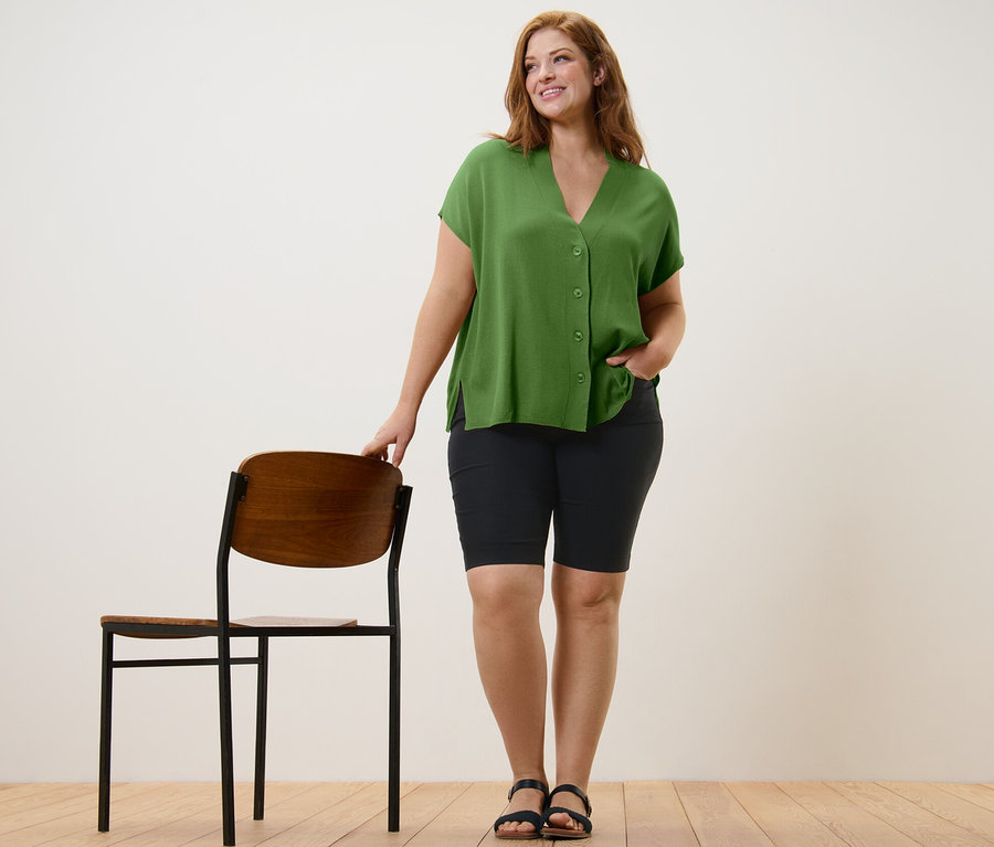 Frau posiert in grünem, kurzärmligem Cardigan und schwarzen Bengalin-Bermudashorts.