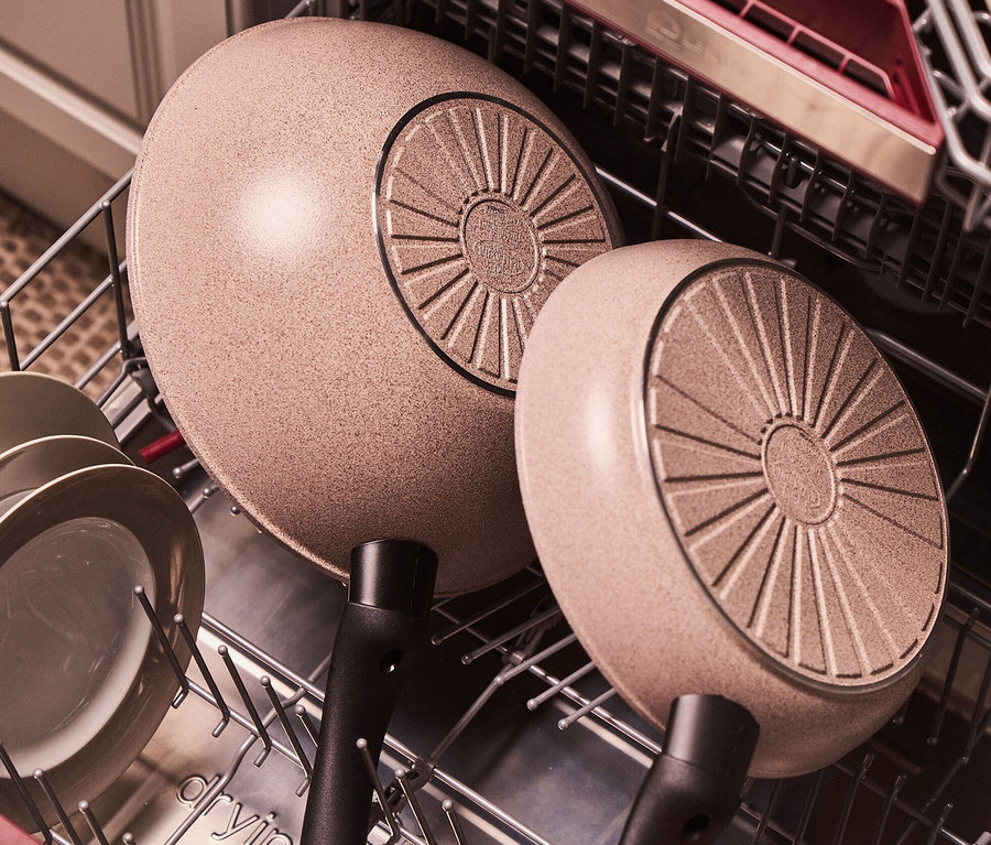 Im Geschirrspüler befinden sich zwei sandfarbene BALLARINI Aluminium-Bratpfannen, 20 und 24 cm.