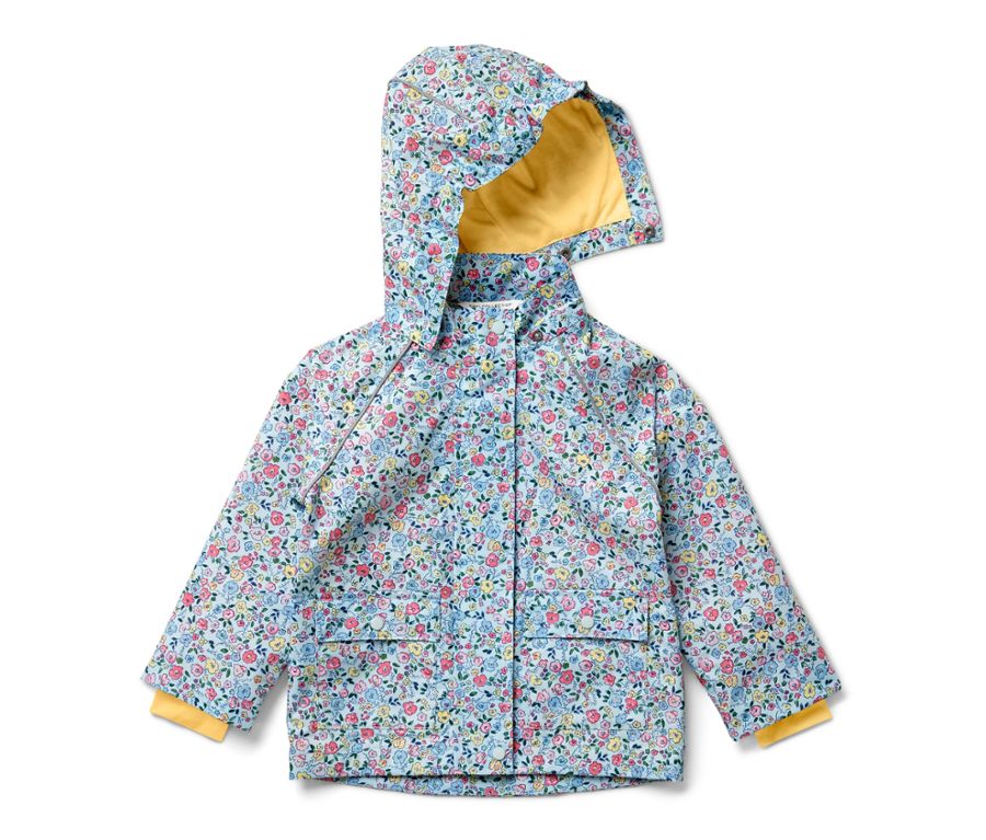 Mädchen steht seitlich und trägt eine geblümte Kinder-Regenjacke, dunkelblaue Hosen und Stiefel.