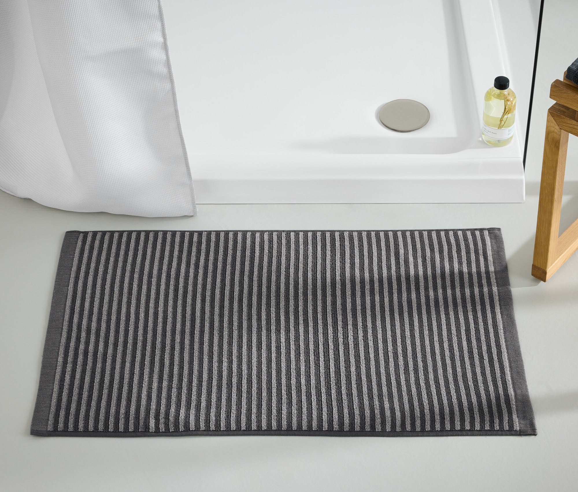 Ein hochwertiger, anthrazitfarbener Duschvorleger liegt vor einer Dusche.