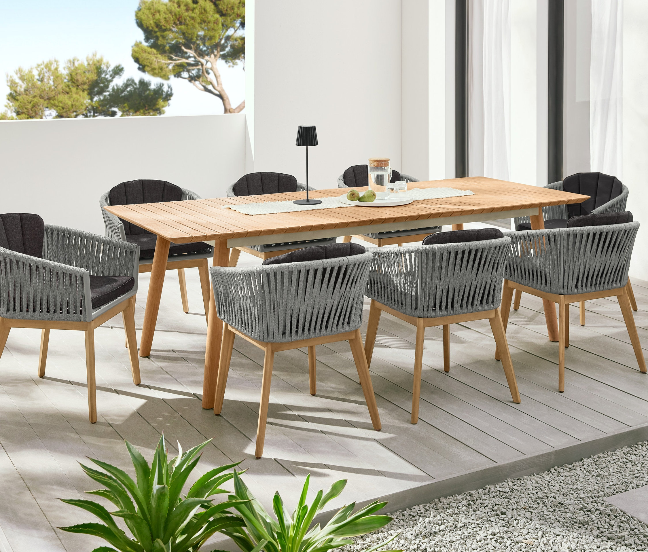 Ein Teak-Ausziehtisch ist von Dining-Sesseln mit Textilgeflecht umgeben. Im Hintergrund stehen zwei Pflanzsäulen »Tinus«.