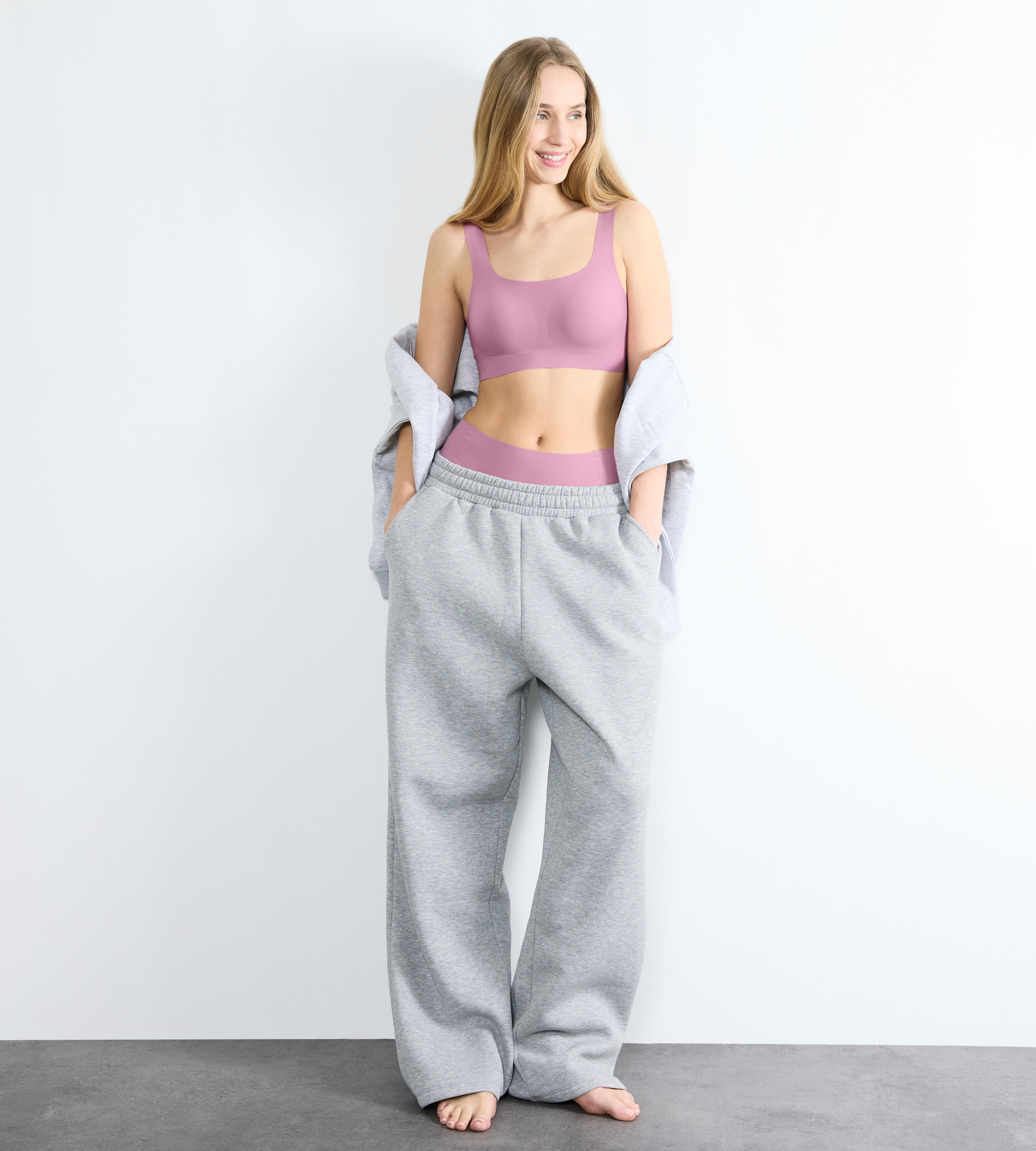 Frau steht und trägt ein lila Sloggi ZERO Feel 2.0 Top und graue Trainingshose.