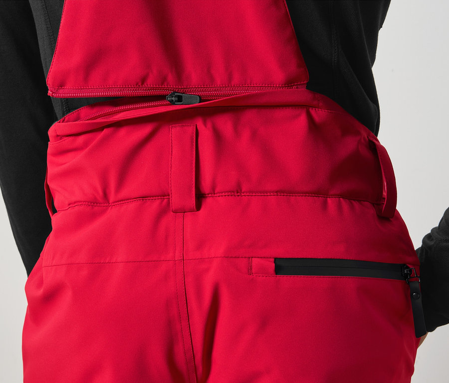 Detail einer roten Latzhose mit schwarzem Reißverschluss.