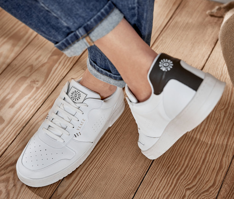 Beine in Jeans und weiße Tchibo x VLACE Coffee Lover Sneaker, Women auf Holzboden.