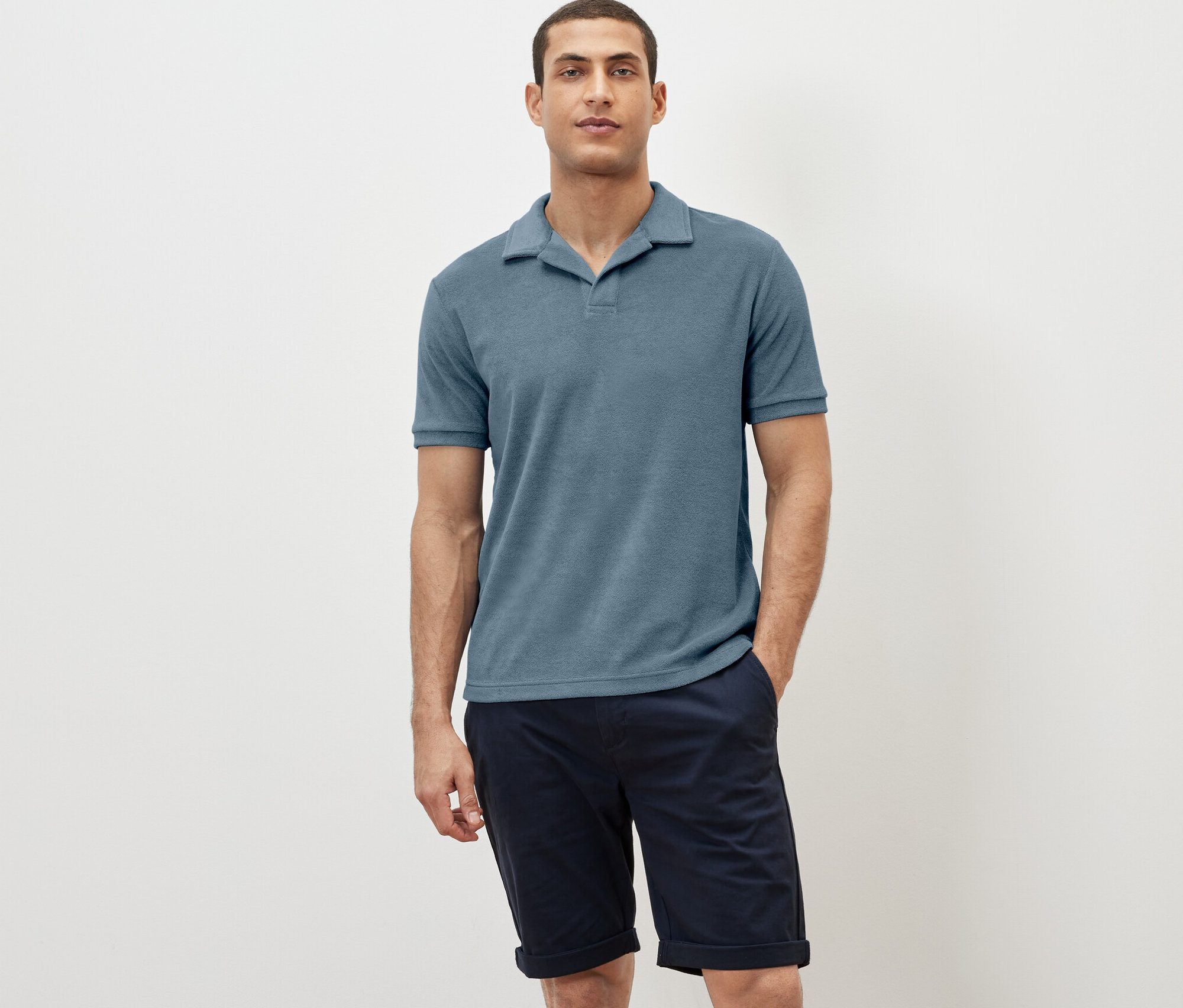 Mann posiert in einem blaugrauen Frottee-Poloshirt und dunkelblauen Shorts.