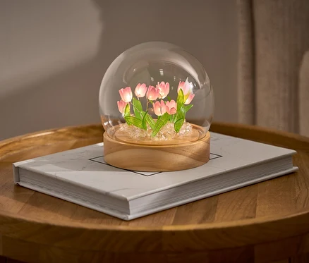 LED-DIY-Bastel-Set mit Tulpen in einer Glaskuppel auf einem Buch auf einem runden Tisch.