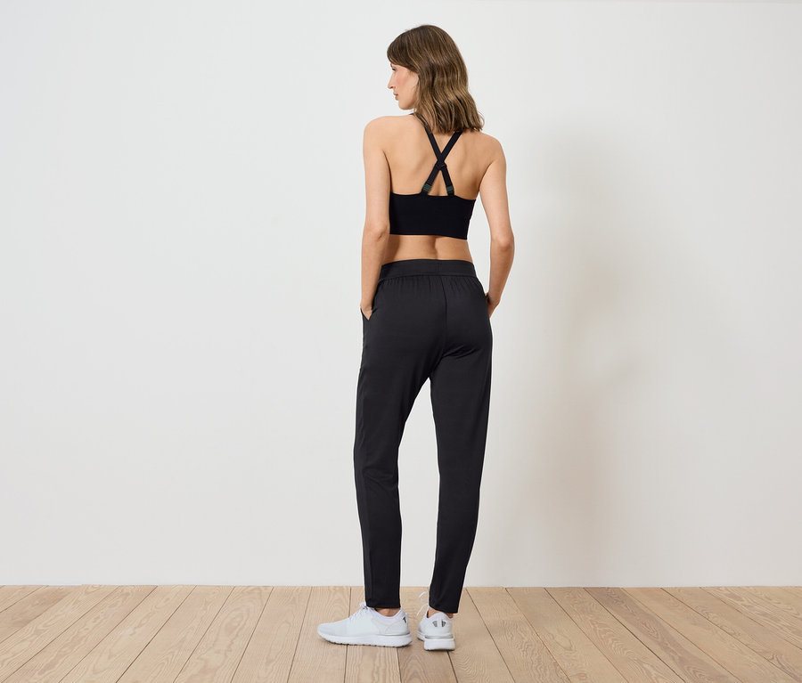 Frau in schwarzem Sporttop und Hose steht mit dem Rücken zur Kamera.