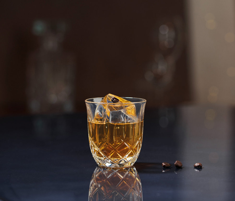 Ein Nachtmann Espressoglas »Noblesse« gefüllt mit einem Getränk und Eiswürfeln steht auf einer dunklen Oberfläche.