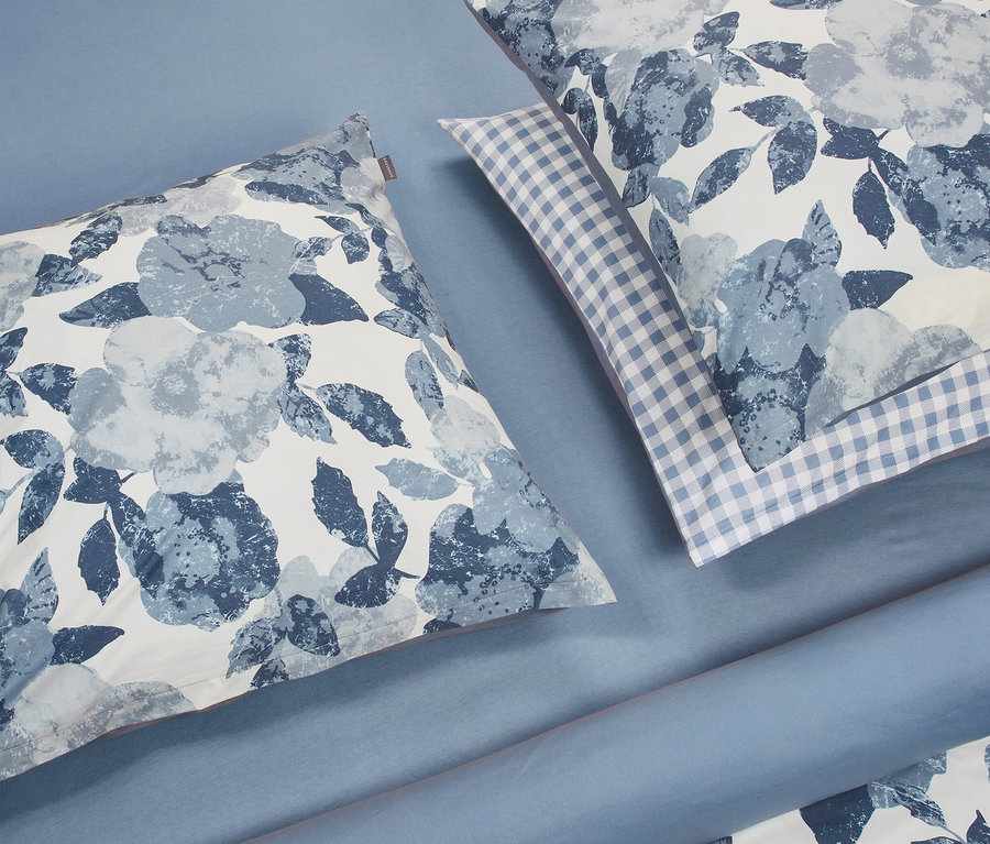 Zwei Kissen und eine Bettdecke mit Blumendruck liegen auf einem blauen Hintergrund. Sichtbar ist ein SCHIESSER Renforcé-Bettwäscheset »Elisa« mit Botanik-Print in hellblau.